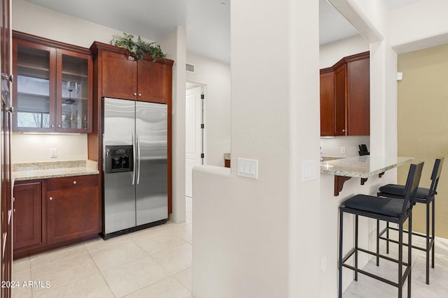 kitchen with light tile patterned floors, light stone counters, a kitchen breakfast bar, and stainless steel fridge with ice dispenser