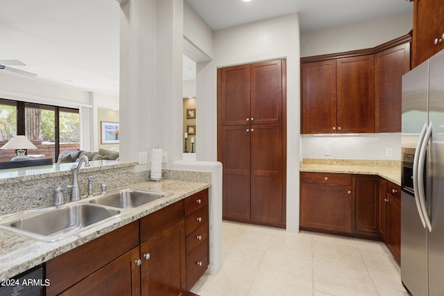 kitchen with light stone counters, ceiling fan, stainless steel fridge, and sink