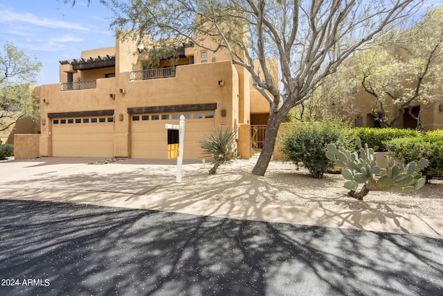 pueblo revival-style home featuring a garage and a balcony