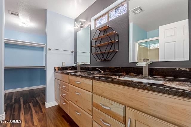 bathroom featuring wood finished floors, a stall shower, a walk in closet, double vanity, and baseboards