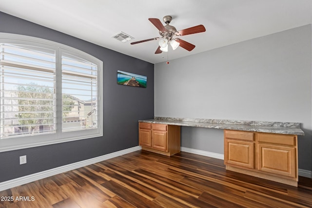 unfurnished office with built in study area, baseboards, dark wood finished floors, ceiling fan, and healthy amount of natural light