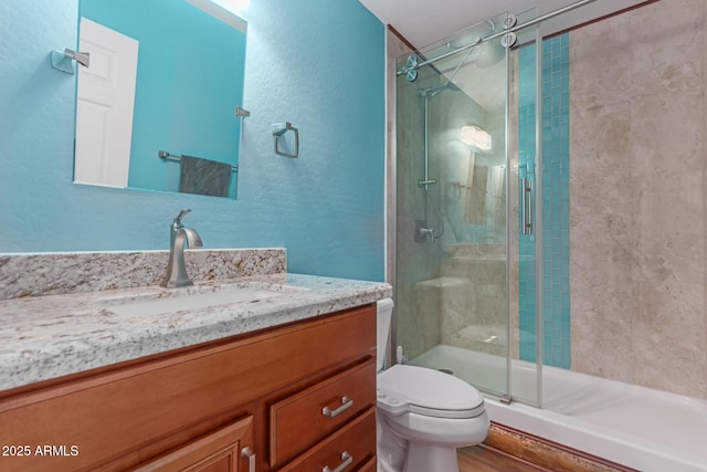 bathroom featuring a stall shower, toilet, a textured wall, and vanity