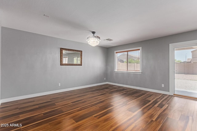 spare room featuring dark wood-style flooring, a chandelier, and baseboards