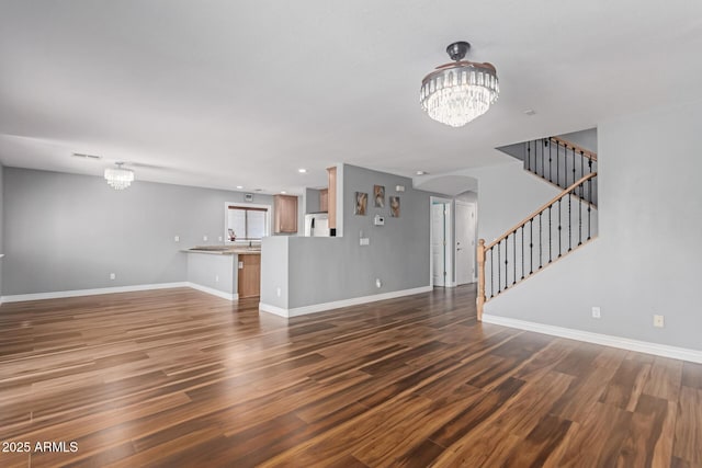 unfurnished living room with a chandelier, dark wood-type flooring, stairs, baseboards, and recessed lighting