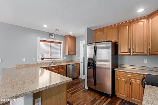 kitchen featuring appliances with stainless steel finishes, a sink, light countertops, dark wood-type flooring, and a peninsula