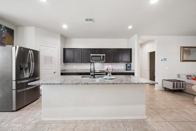 kitchen featuring appliances with stainless steel finishes, a center island with sink, sink, and light stone counters