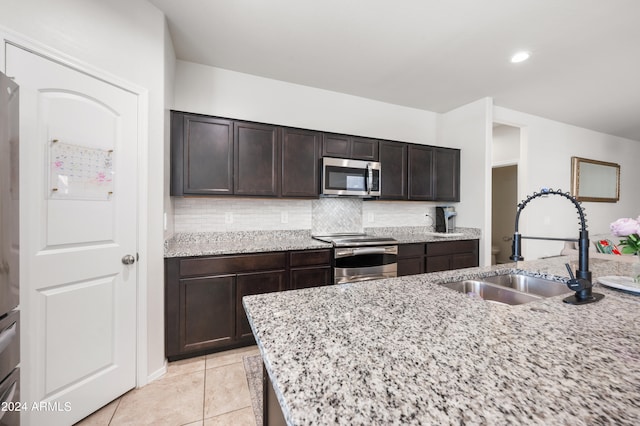 kitchen with appliances with stainless steel finishes, light stone counters, light tile patterned floors, dark brown cabinets, and sink