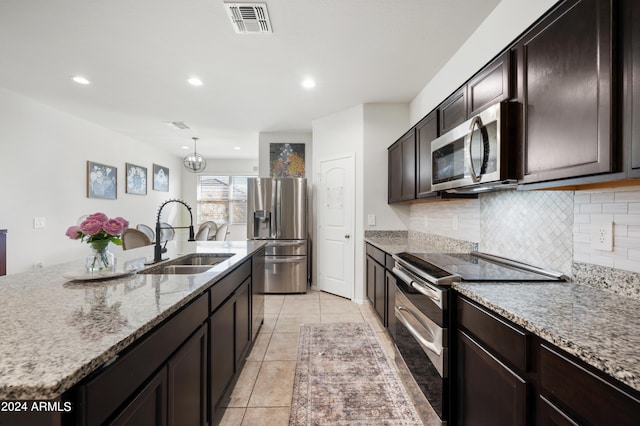 kitchen with light tile patterned flooring, stainless steel appliances, an inviting chandelier, a kitchen island with sink, and sink