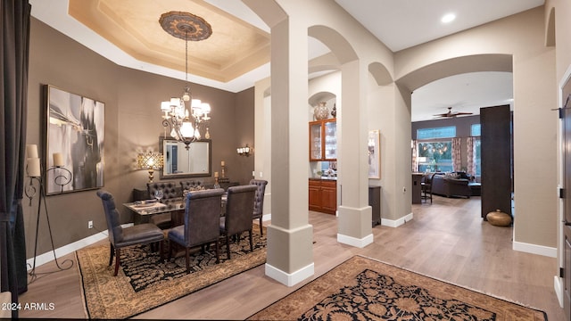 dining room featuring ceiling fan with notable chandelier, light hardwood / wood-style flooring, and a tray ceiling