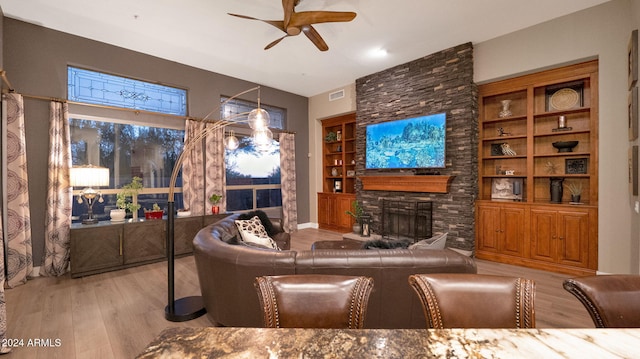 living room featuring ceiling fan, built in shelves, a fireplace, and light hardwood / wood-style flooring