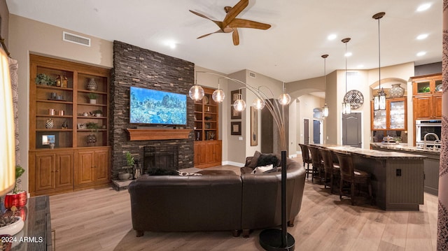 living room featuring ceiling fan, light hardwood / wood-style floors, a stone fireplace, and sink