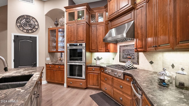 kitchen featuring wall chimney exhaust hood, stainless steel appliances, sink, dark stone countertops, and light hardwood / wood-style floors