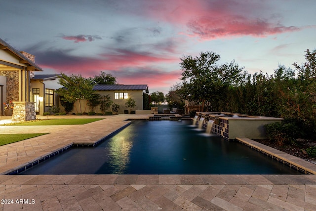 pool at dusk featuring an in ground hot tub, pool water feature, and a patio