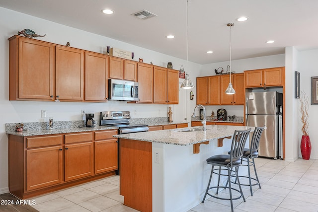 kitchen featuring pendant lighting, light stone counters, sink, an island with sink, and stainless steel appliances