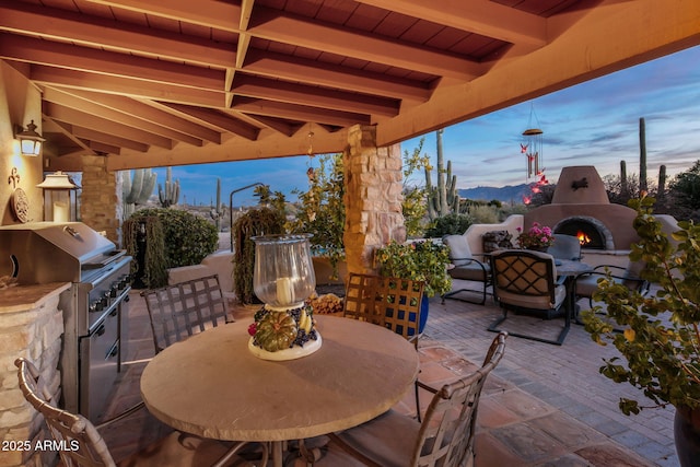 patio terrace at dusk featuring a mountain view, area for grilling, exterior fireplace, and exterior kitchen