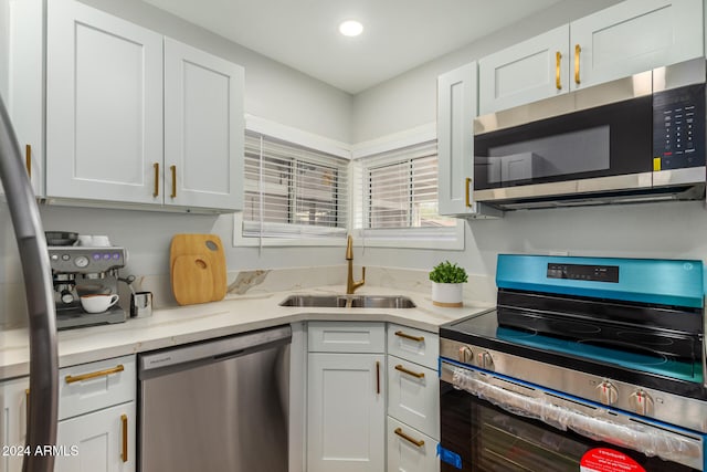 kitchen with white cabinets, appliances with stainless steel finishes, light stone counters, and sink