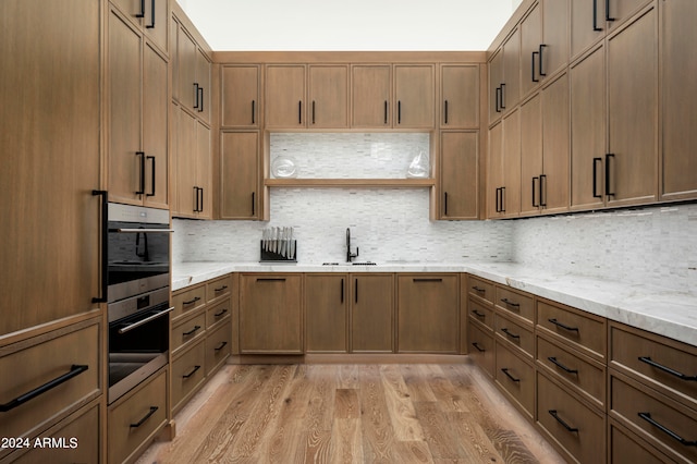 kitchen with decorative backsplash, light hardwood / wood-style floors, light stone counters, and sink