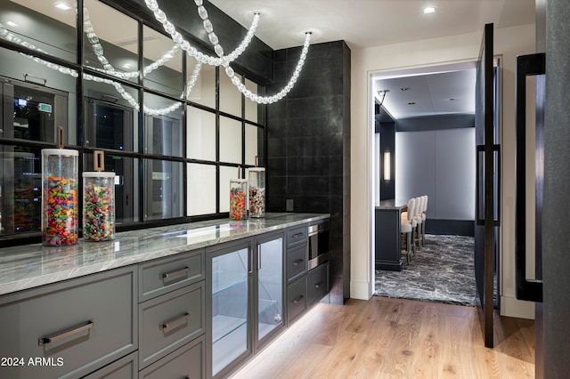 bar featuring gray cabinets, light stone counters, and light hardwood / wood-style floors