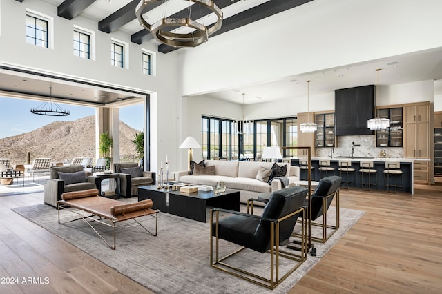 living room featuring sink, a mountain view, a towering ceiling, a chandelier, and light hardwood / wood-style floors