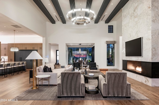 living room featuring a large fireplace, wood-type flooring, beamed ceiling, a high ceiling, and a chandelier