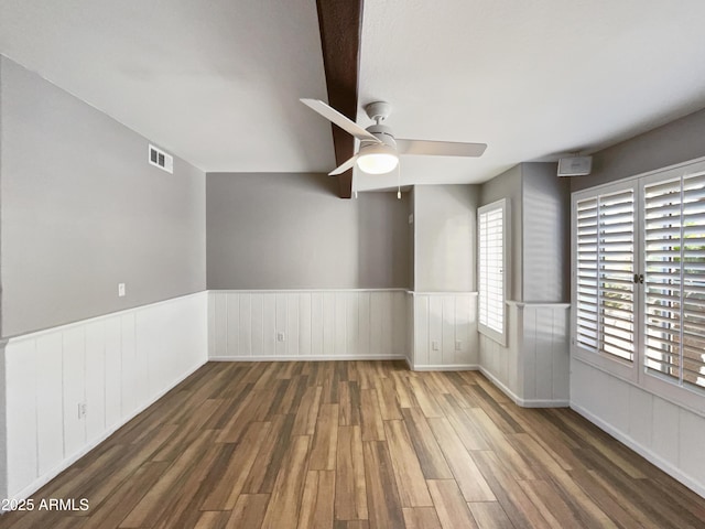 spare room featuring dark wood-type flooring, a wainscoted wall, visible vents, and a ceiling fan