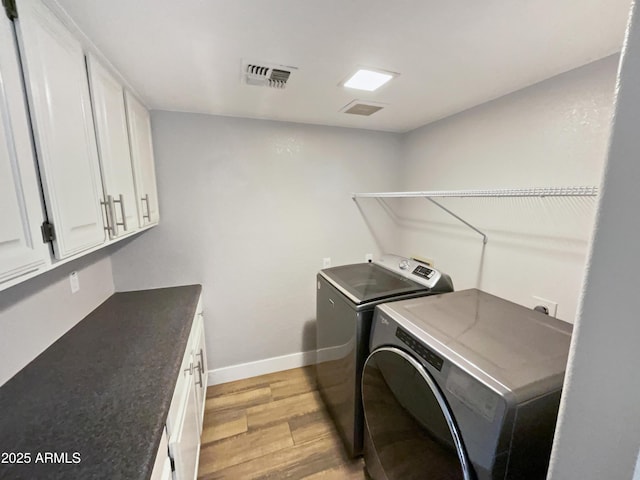 laundry room featuring light wood finished floors, washing machine and clothes dryer, visible vents, cabinet space, and baseboards