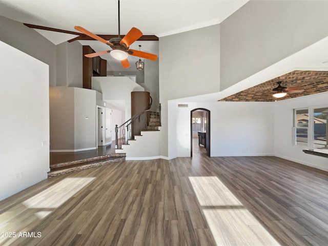 unfurnished living room with arched walkways, crown molding, stairway, ceiling fan, and wood finished floors