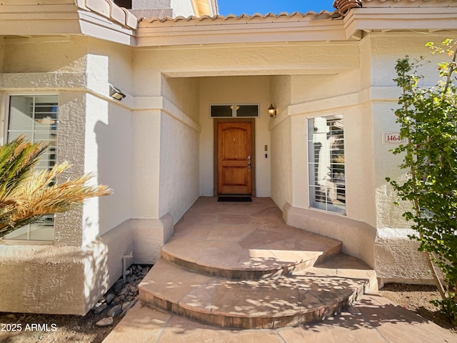 view of exterior entry with a tile roof and stucco siding