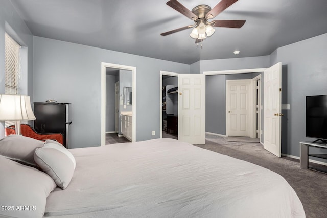 bedroom with baseboards, a ceiling fan, connected bathroom, carpet, and a walk in closet