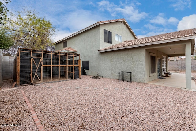 back of house with an outbuilding, stucco siding, fence, exterior structure, and a tiled roof