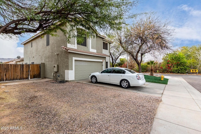 view of home's exterior with an attached garage, fence, a tile roof, driveway, and stucco siding