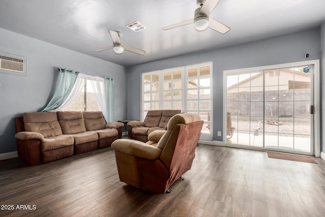 living room with dark wood-style floors, visible vents, baseboards, and a ceiling fan