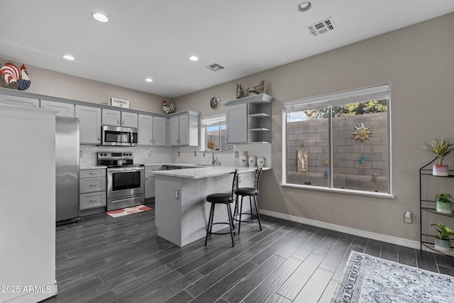 kitchen with sink, a breakfast bar area, appliances with stainless steel finishes, backsplash, and kitchen peninsula