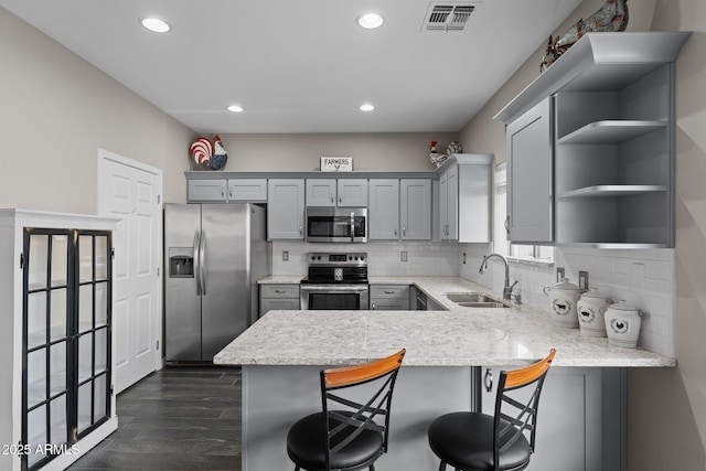 kitchen with sink, a breakfast bar area, gray cabinetry, appliances with stainless steel finishes, and kitchen peninsula