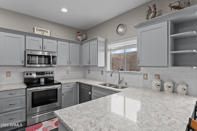 kitchen with sink, tasteful backsplash, gray cabinets, stainless steel appliances, and light stone countertops