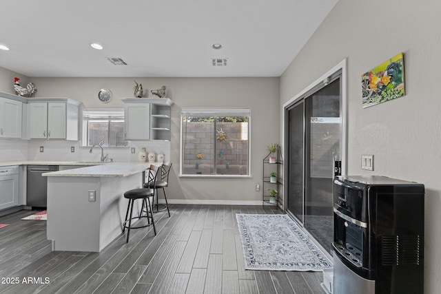 kitchen featuring backsplash, dark hardwood / wood-style flooring, a kitchen bar, stainless steel dishwasher, and light stone countertops