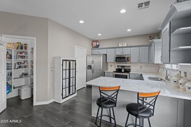 kitchen with gray cabinets, appliances with stainless steel finishes, sink, a kitchen bar, and kitchen peninsula