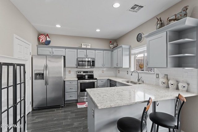 kitchen featuring sink, a breakfast bar area, light stone counters, appliances with stainless steel finishes, and kitchen peninsula