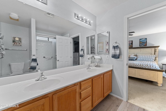 bathroom featuring hardwood / wood-style flooring, tiled shower, vanity, and toilet