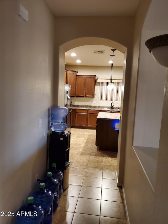 kitchen with hanging light fixtures, stainless steel refrigerator with ice dispenser, sink, and light tile patterned floors