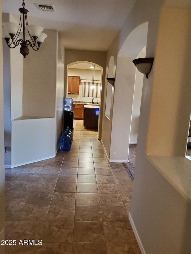 corridor with an inviting chandelier, sink, and dark tile patterned floors