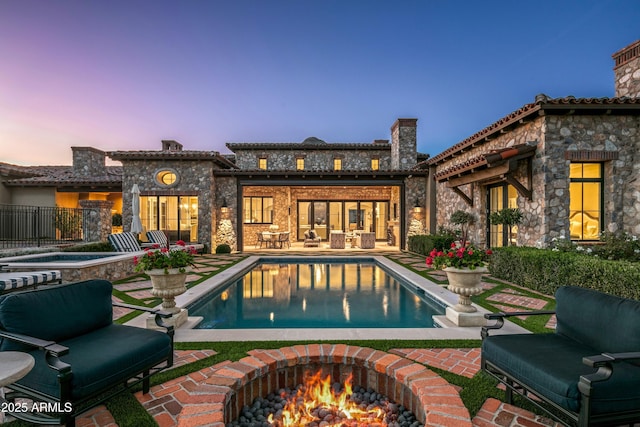 back house at dusk with a pool with hot tub, a patio, and an outdoor fire pit