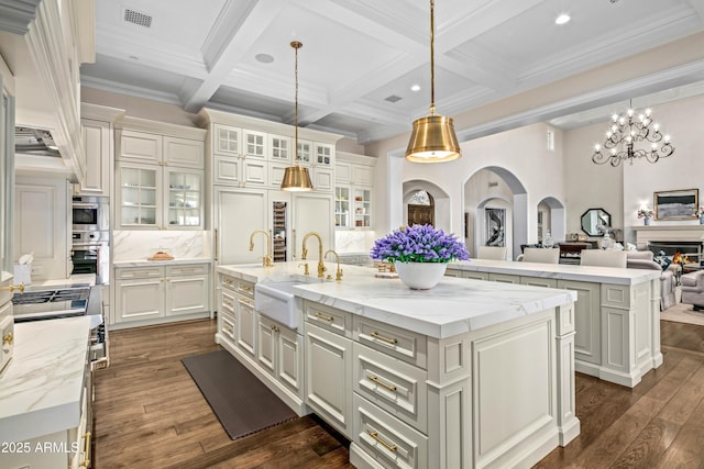 kitchen with sink, a large island with sink, backsplash, hanging light fixtures, and coffered ceiling