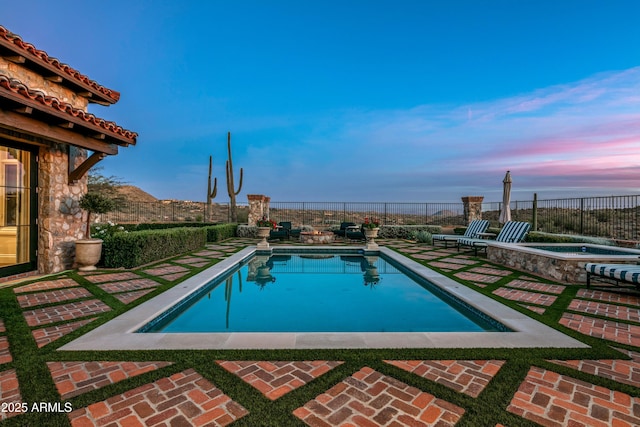 pool at dusk with an in ground hot tub and a patio area