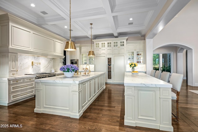 kitchen with decorative light fixtures, light stone countertops, a kitchen island with sink, and backsplash