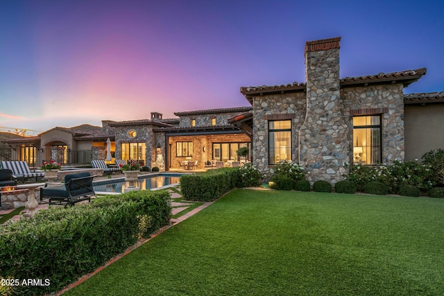 back house at dusk with a patio area and a yard