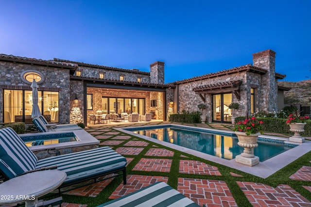 back house at dusk featuring a pool with hot tub, french doors, and a patio area