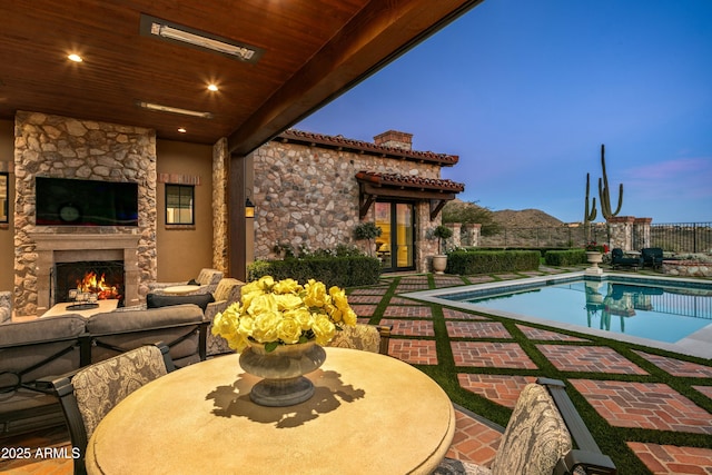 pool at dusk featuring a patio area and an outdoor stone fireplace