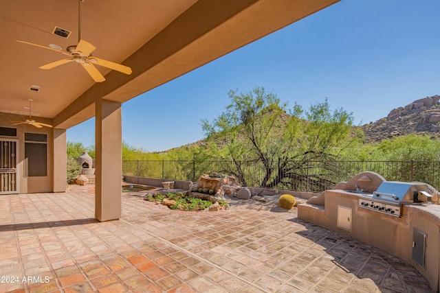 view of patio with a ceiling fan, a fireplace, an outdoor kitchen, and fence