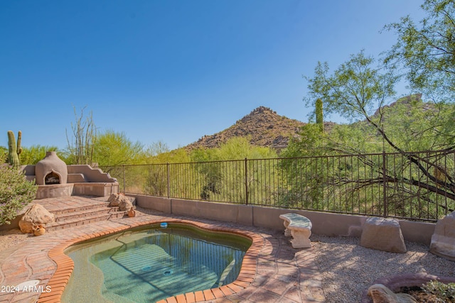 view of swimming pool with a patio area, fence, an outdoor fireplace, and a mountain view